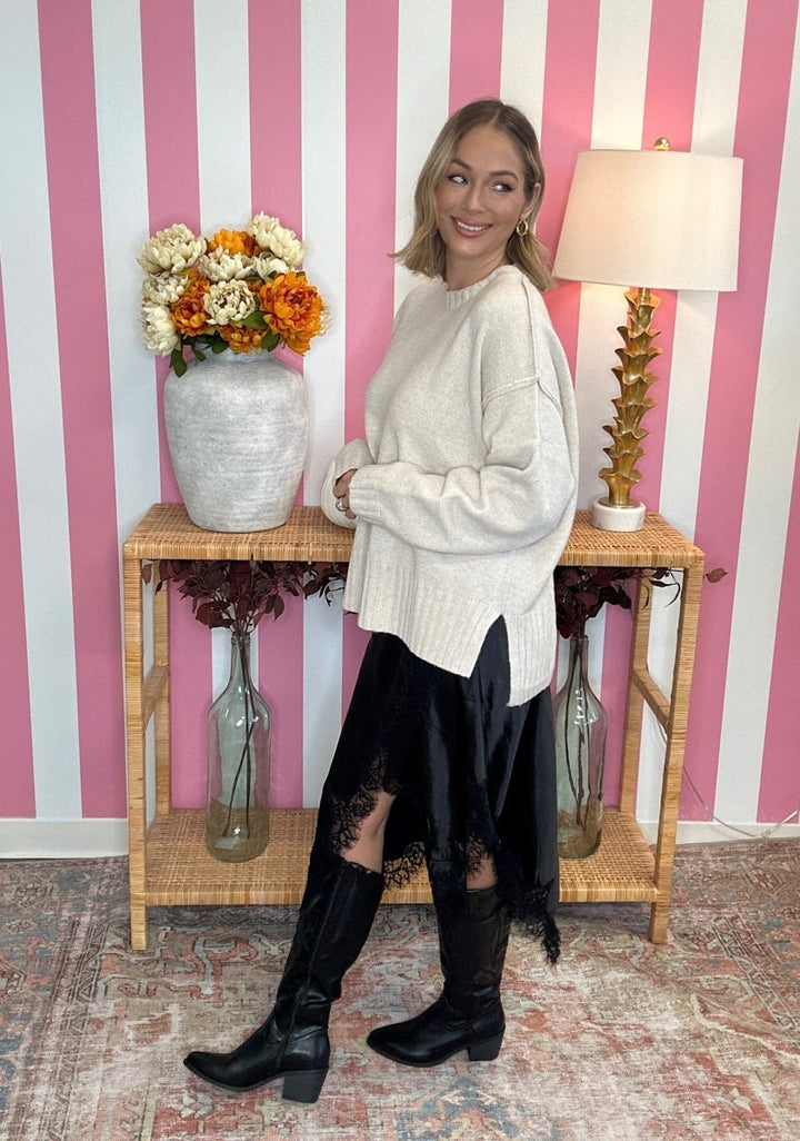 woman standing in a white sweater with a black lace skirt