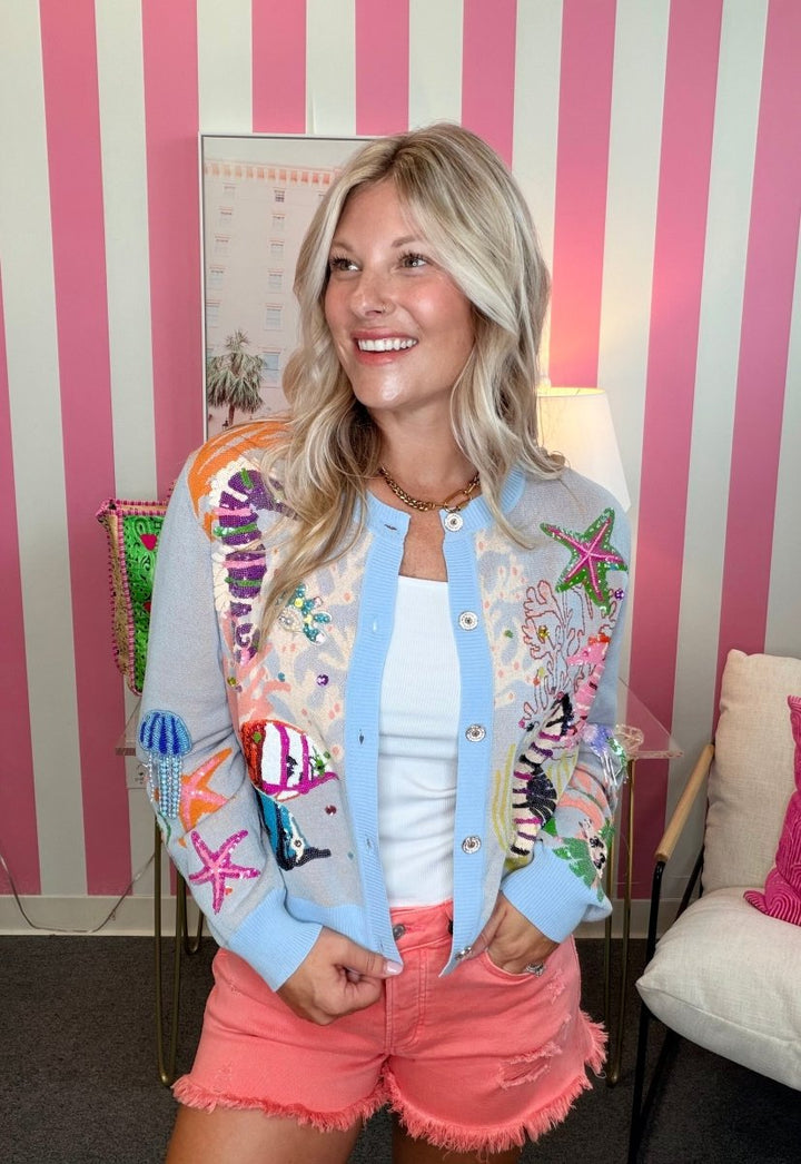 Woman wearing a colorful embroidered jacket and pink shorts in a room with striped walls.