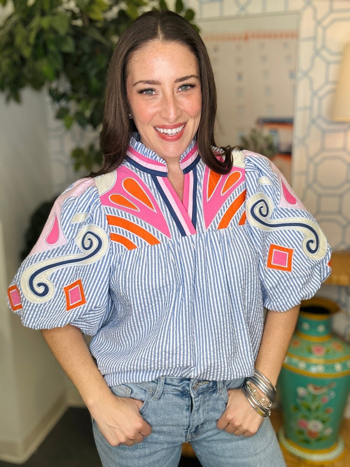 Woman wearing a colorful blouse with puffed sleeves in an indoor setting.