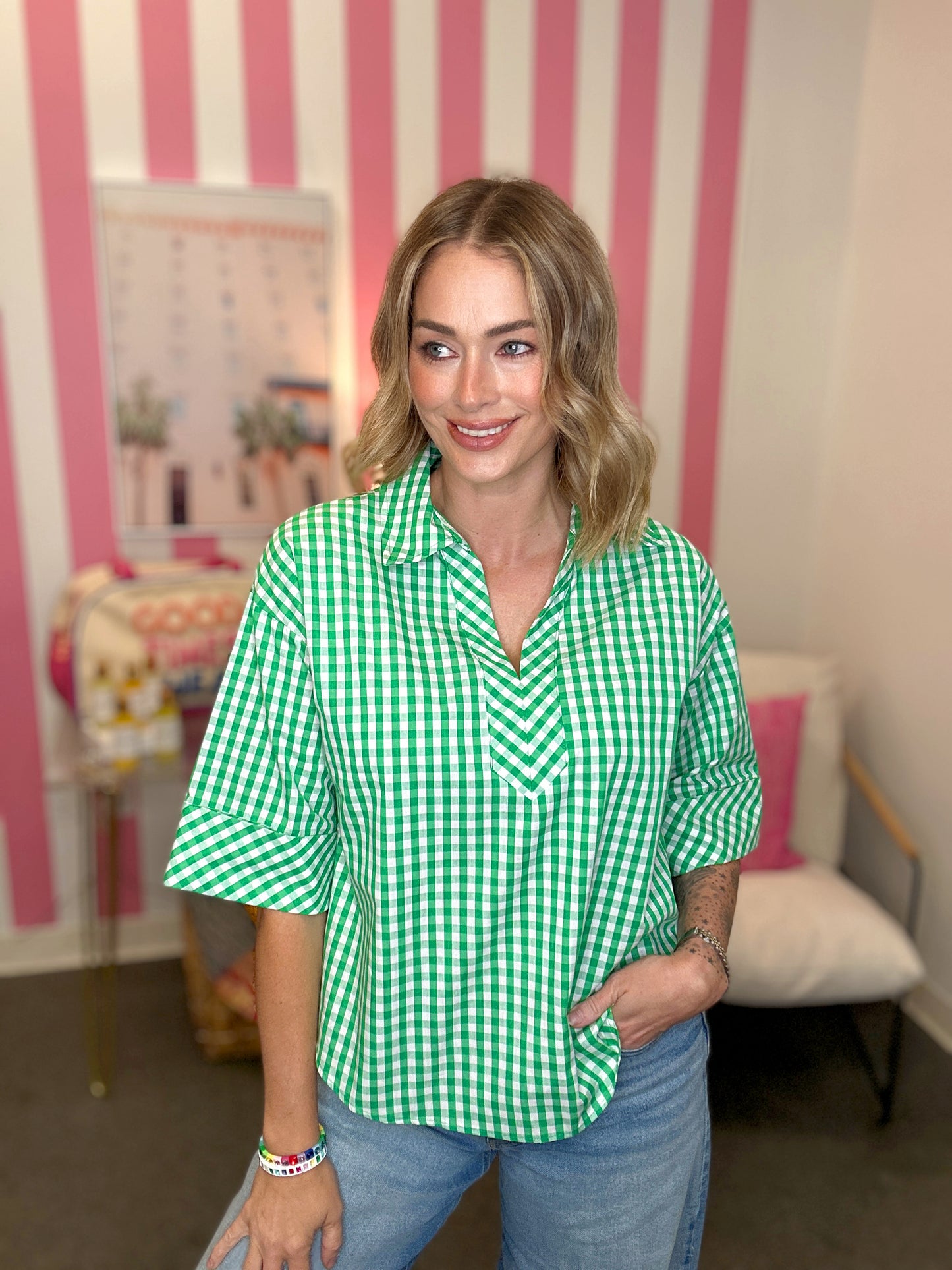 Woman wearing a green checkered shirt in a room with pink and white striped walls.