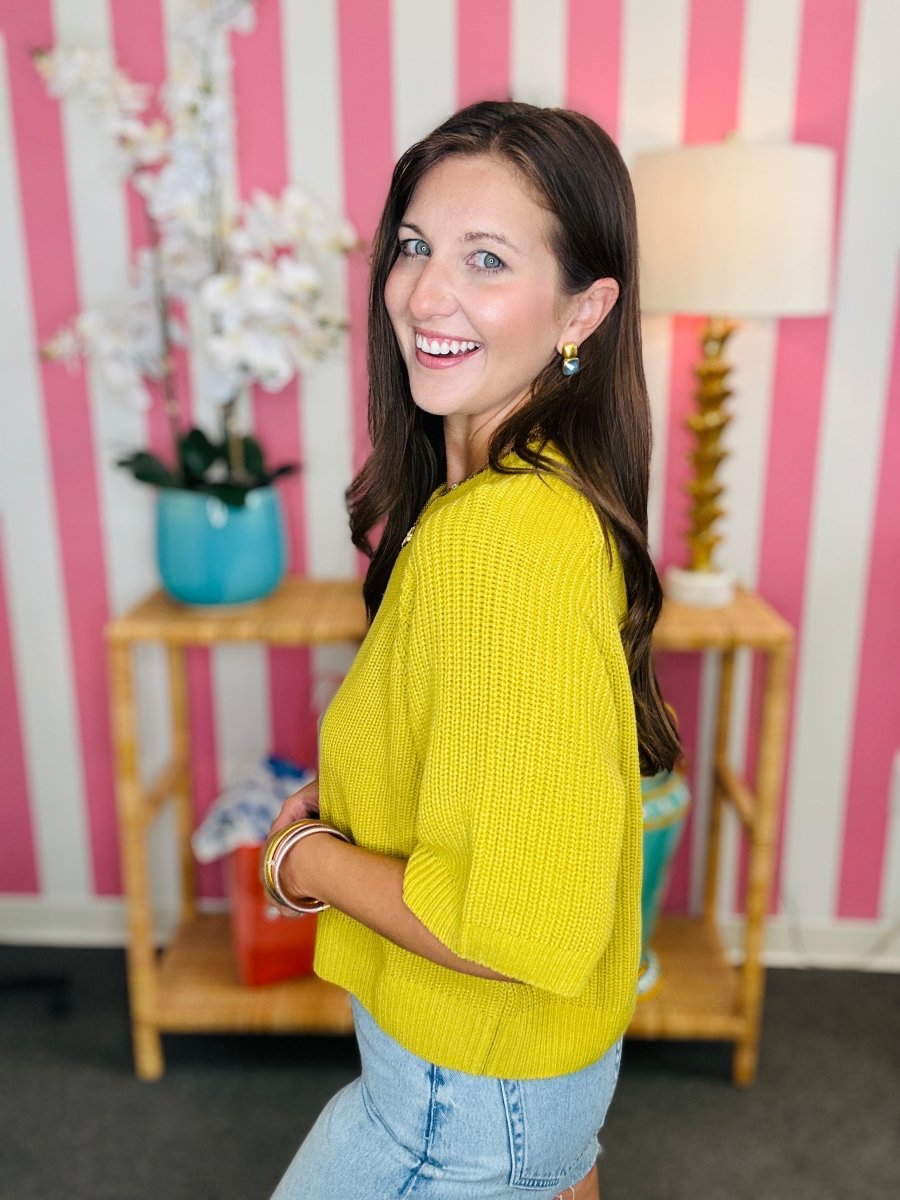 Woman wearing a yellow sweater in a room with striped walls and decor.
