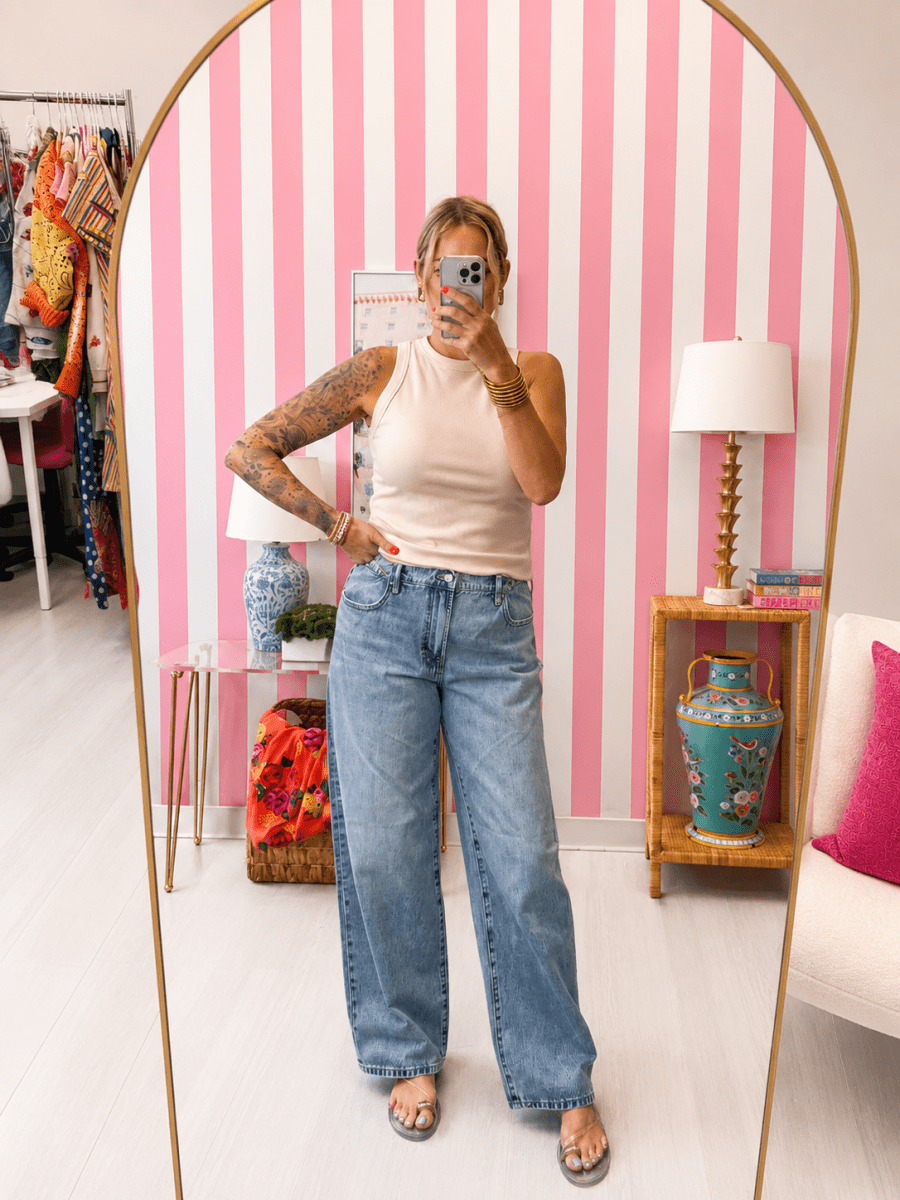 Person taking a mirror selfie in a room with pink and white striped wallpaper.