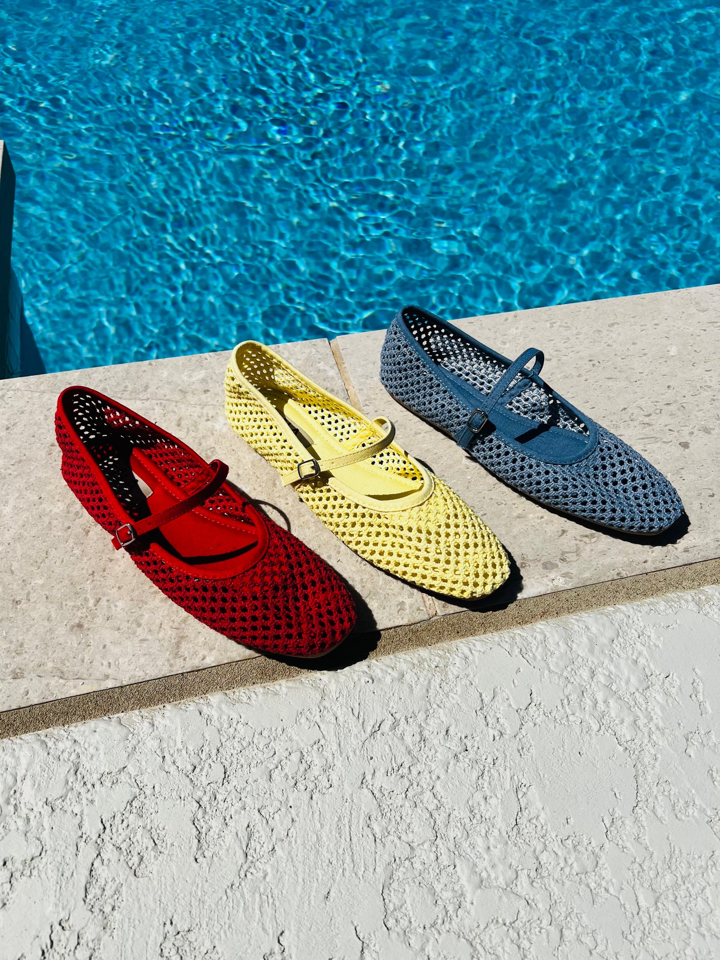 Three colorful shoes (red, yellow, blue) on a ledge by a pool.