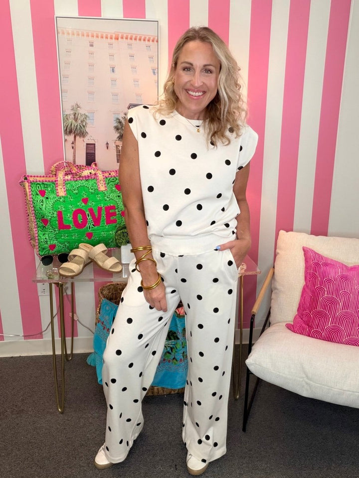 Woman in a polka dot outfit standing in a room with a striped wall and a chair.