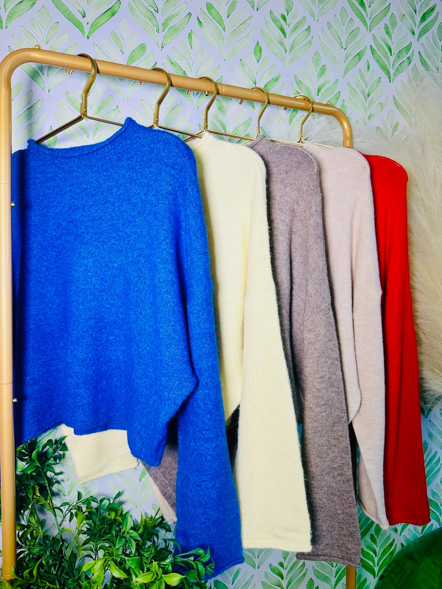 Colorful sweaters hanging on a rack against a leaf-patterned wall.
