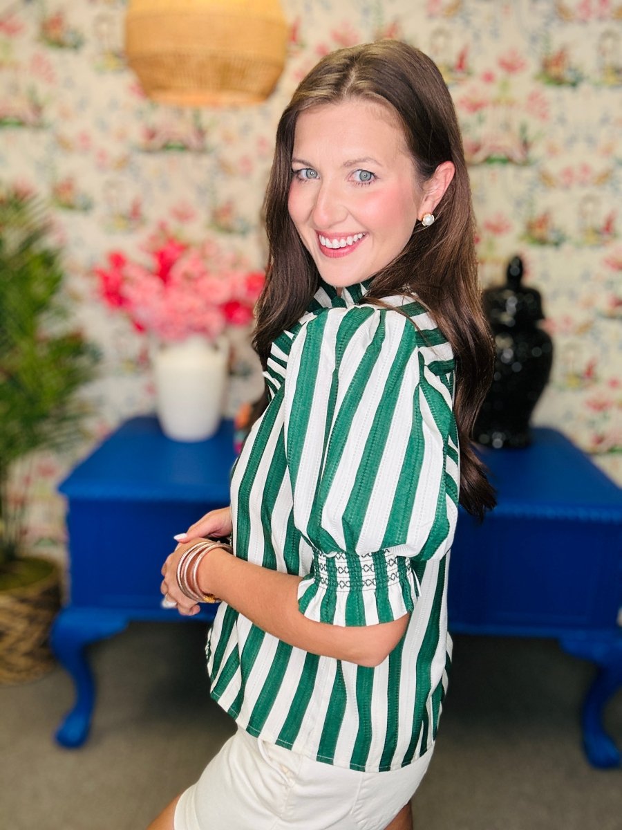 Woman wearing a green and white striped shirt in a room with floral wallpaper and blue furniture.