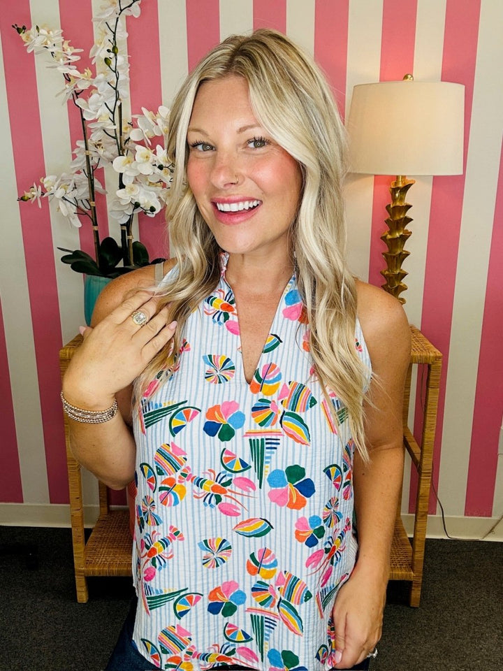 Woman wearing a colorful floral dress in a room with striped wallpaper.