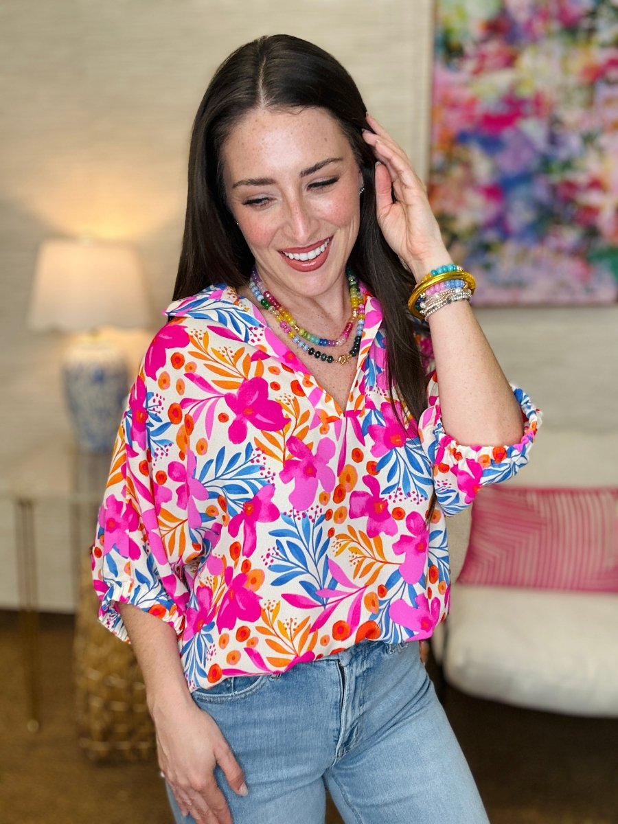 Woman wearing a colorful floral blouse in a room with a lamp and painting.
