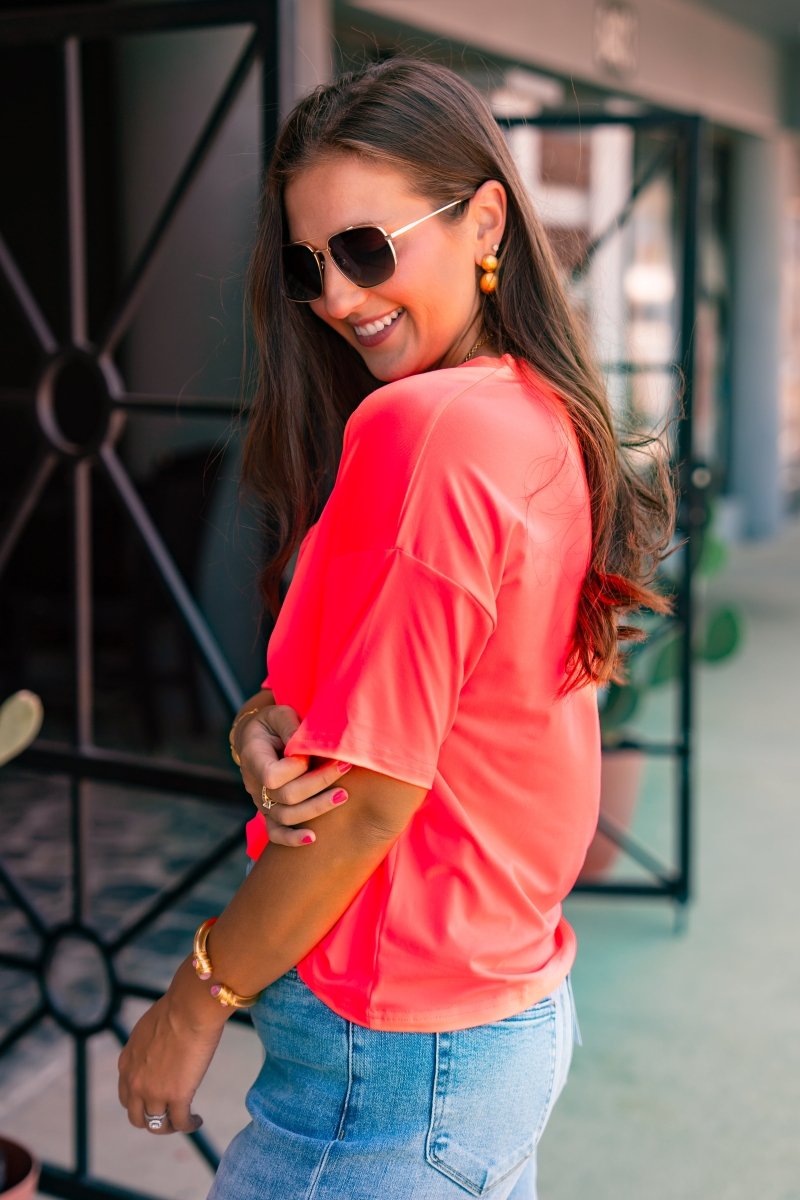 Woman wearing a bright pink top and blue jeans, standing indoors.