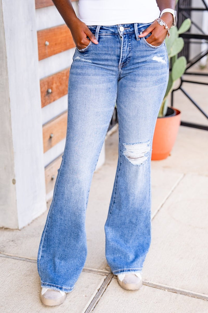 Person wearing light blue flared jeans with a white top and silver shoes indoors.