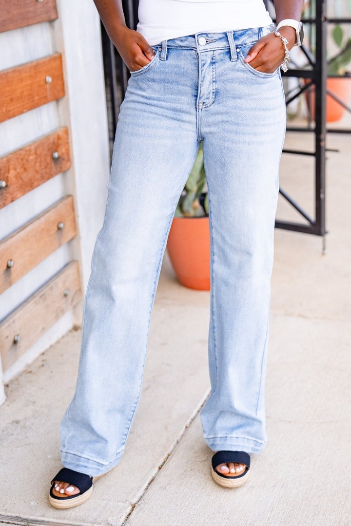 Person wearing light blue jeans standing on a sidewalk.