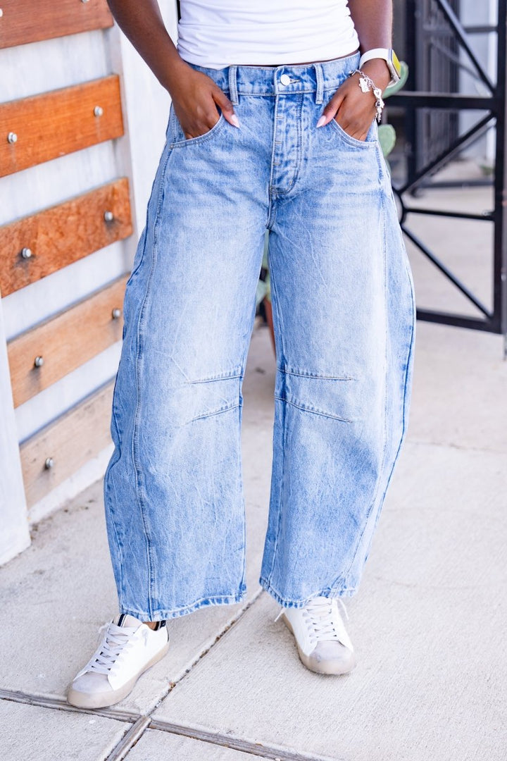 Person wearing light blue wide-leg jeans and white sneakers on a sidewalk.