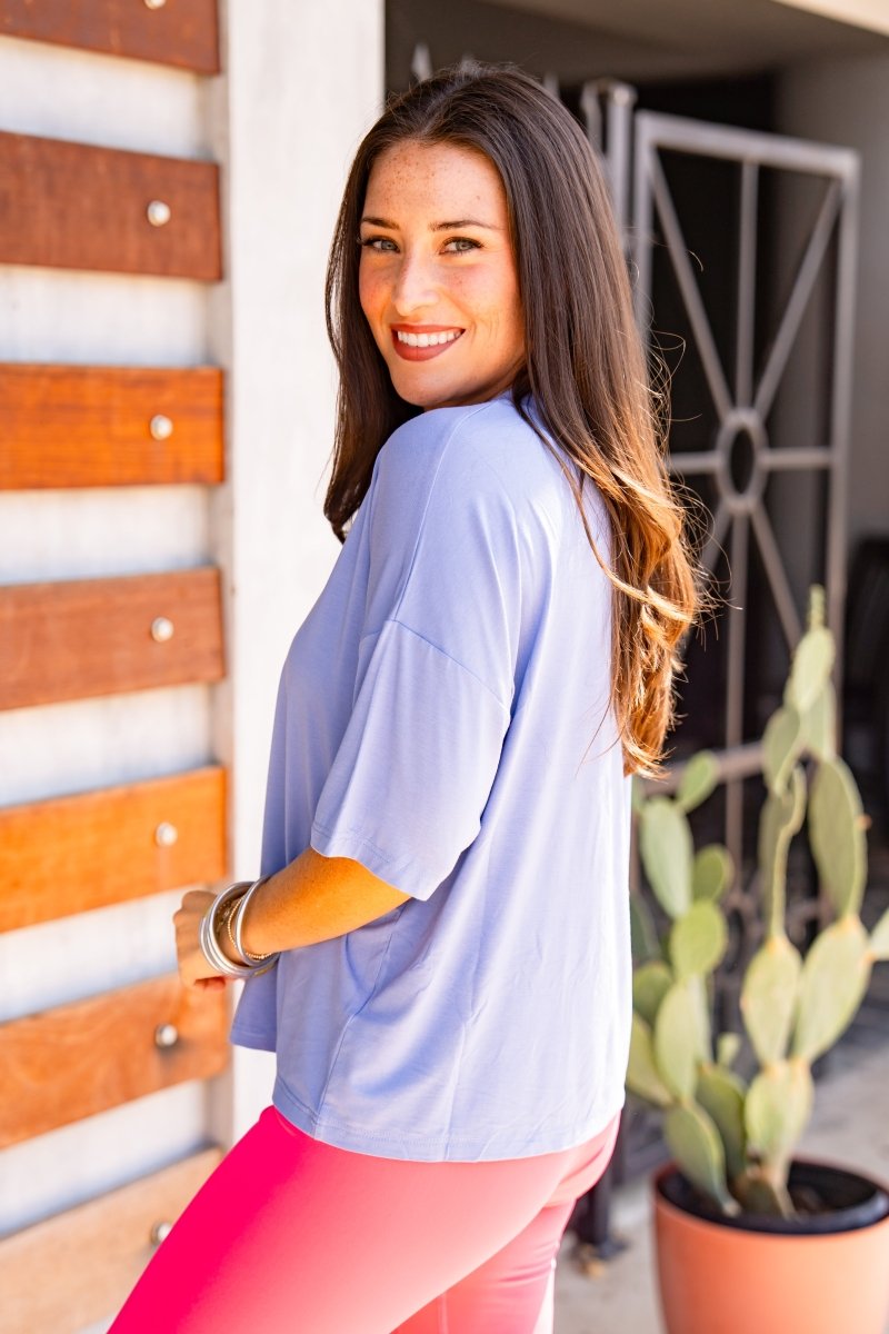 Woman in a blue shirt and pink pants standing outdoors with a cactus plant in the background.
