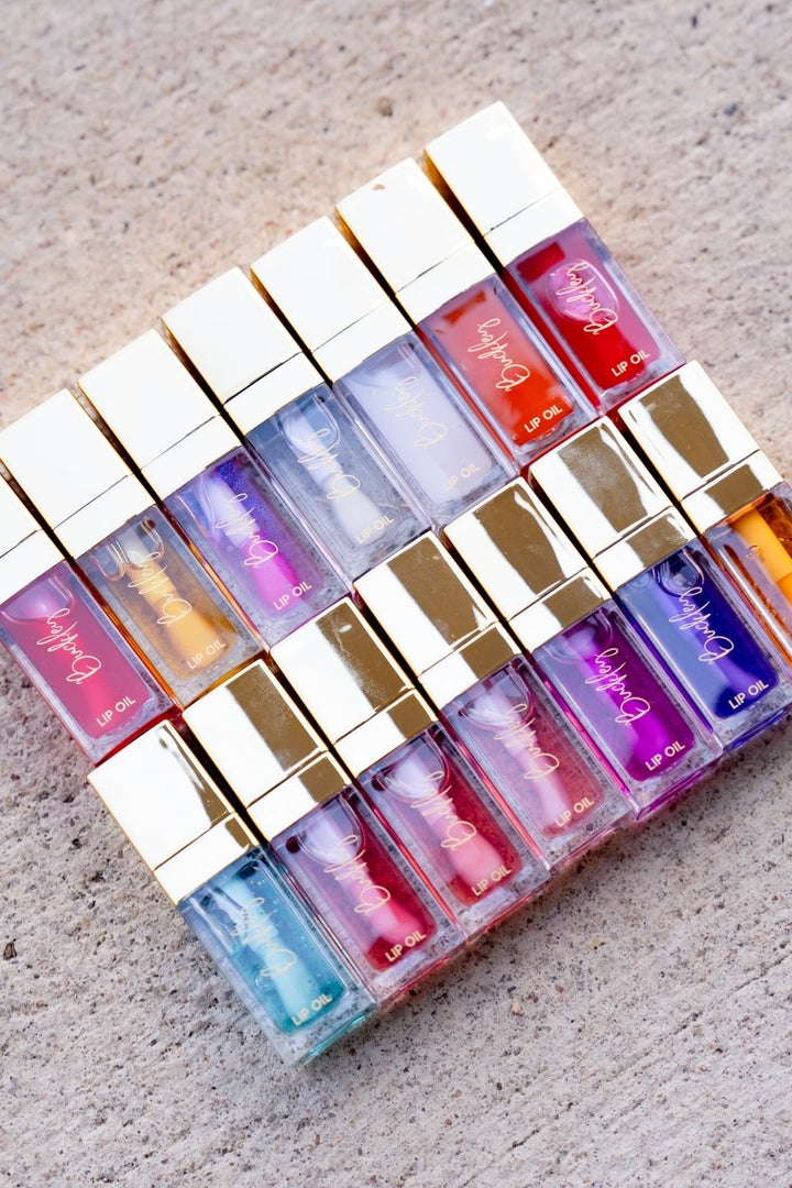 Set of colorful lip glosses in a decorative holder on a textured surface