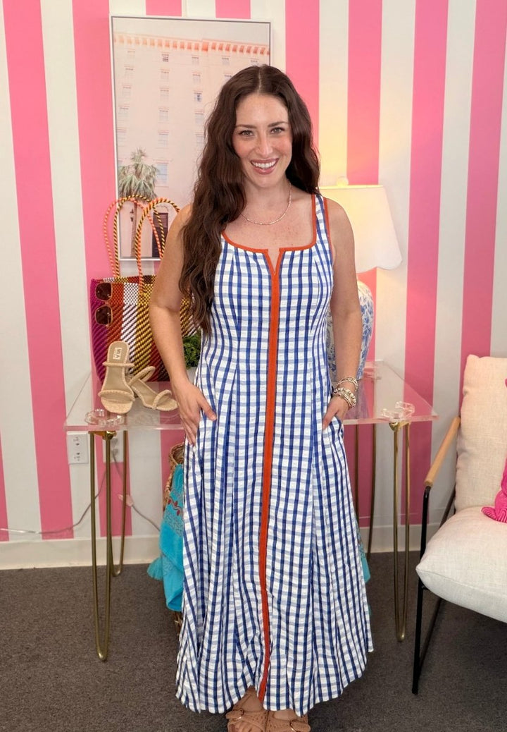 Woman in a blue checkered dress standing in a room with striped walls and furniture.