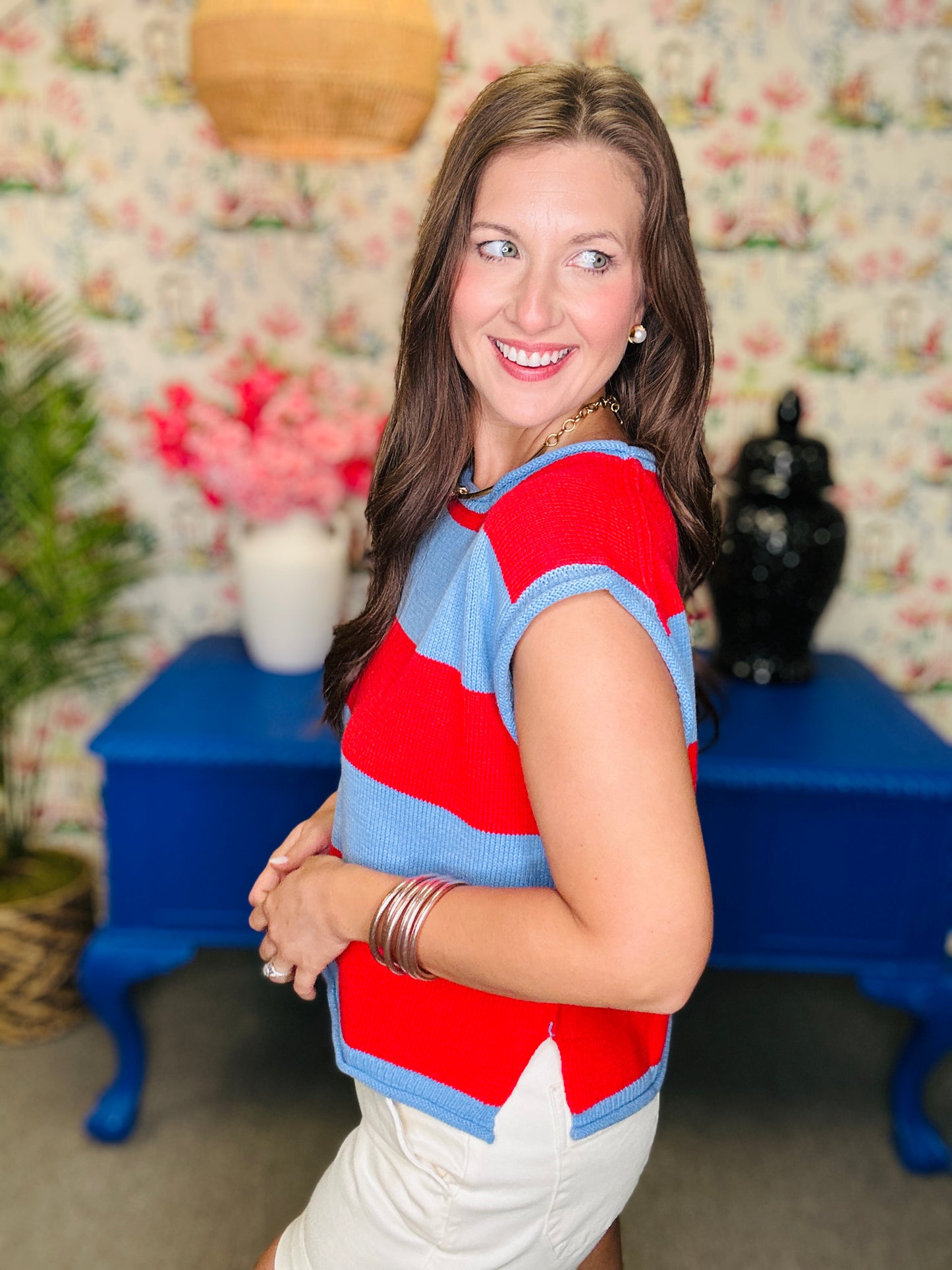 Woman wearing a red and blue striped shirt with a floral wall and blue table in the background