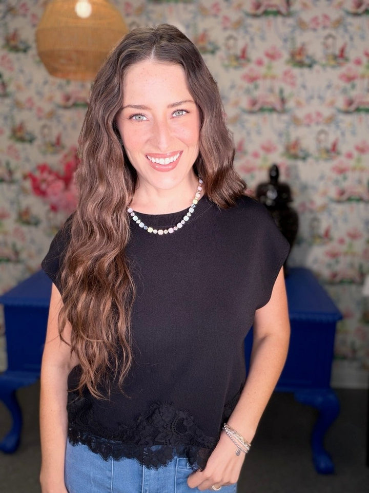 Woman wearing a black top with lace details in a room with floral wallpaper.
