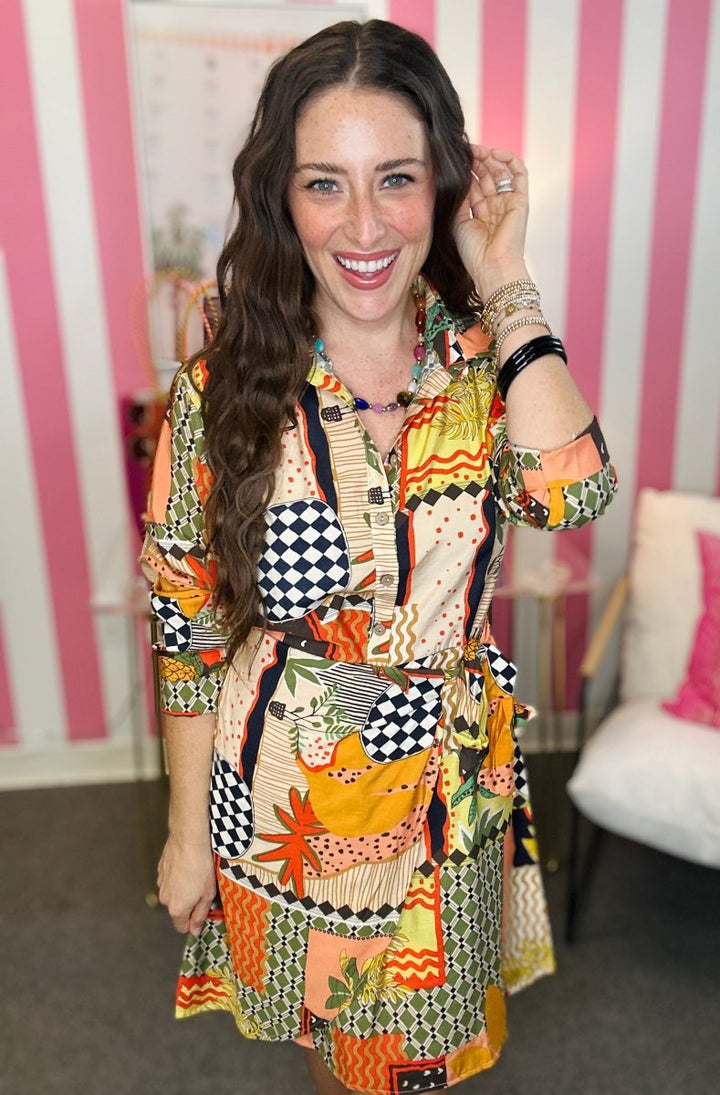 Woman wearing a colorful patterned dress in an indoor setting with pink and white striped walls.