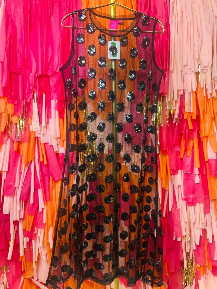 Dress with black polka dots on a hanger against a colorful fringe background