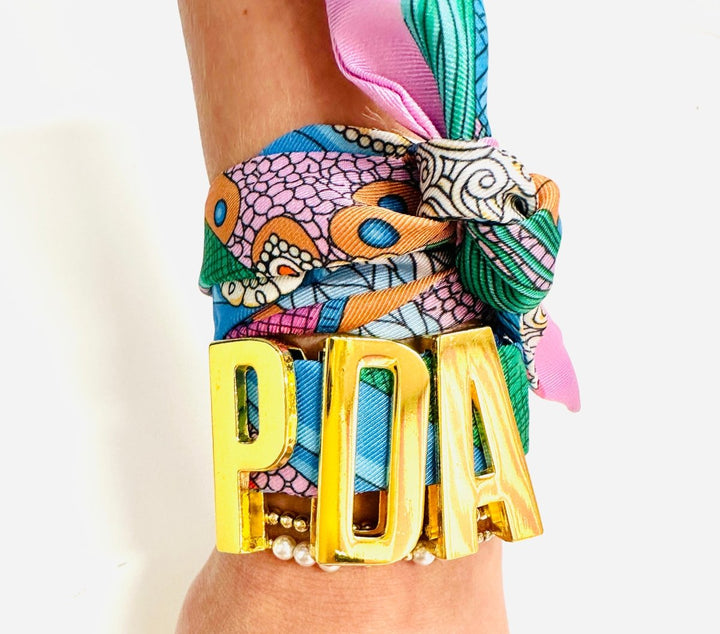 Colorful scarf with 'PDA' letters worn around a wrist on a white background