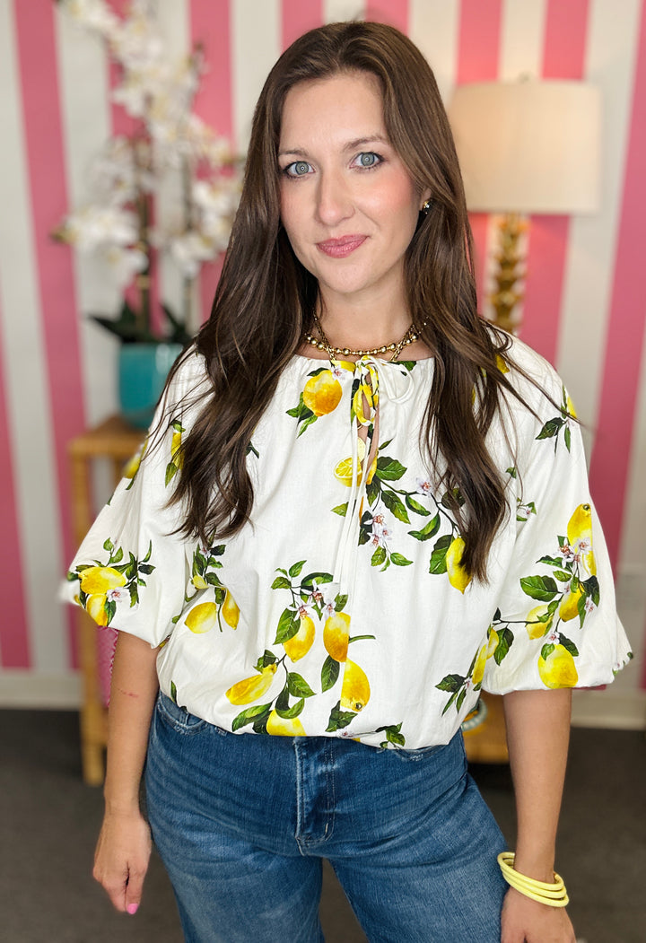 Woman wearing a white blouse with lemon print in a room with pink and white striped wallpaper.
