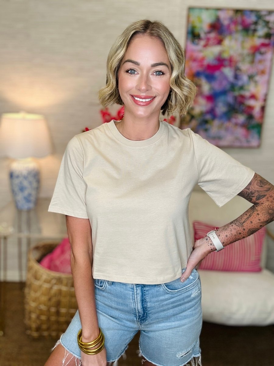 Woman wearing a beige t-shirt and denim shorts in a living room setting.