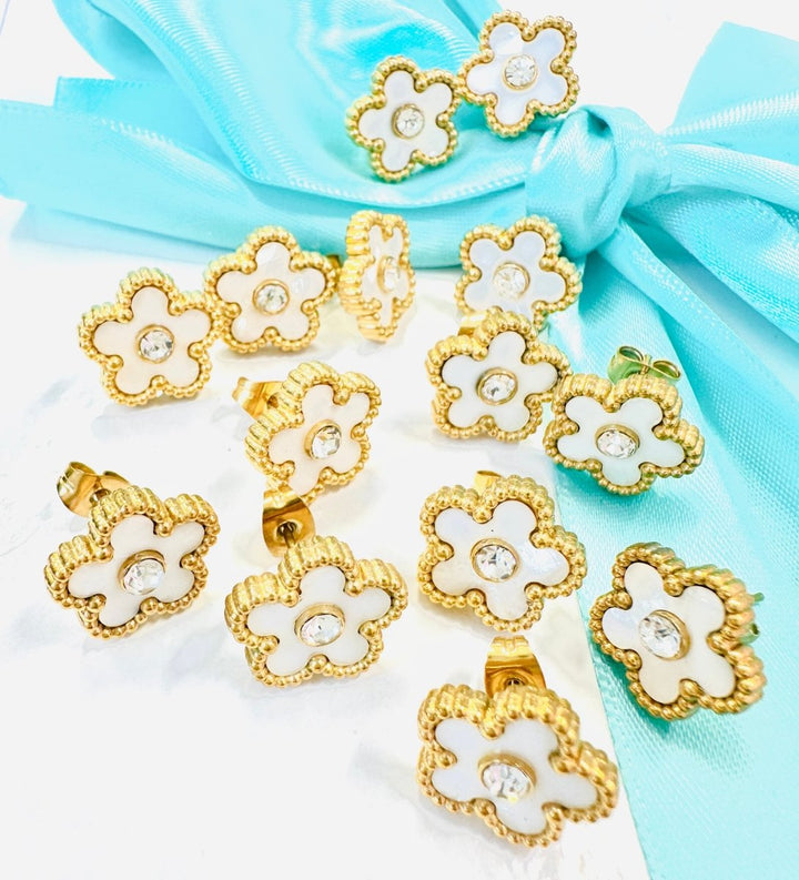 Gold and white floral earrings on a light blue fabric background