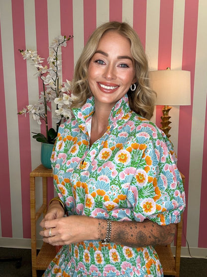 Woman wearing a colorful floral dress in a room with striped wallpaper.