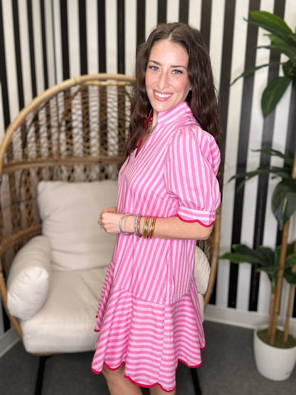 Woman wearing a pink and white striped dress in a room with a wicker chair and plant.
