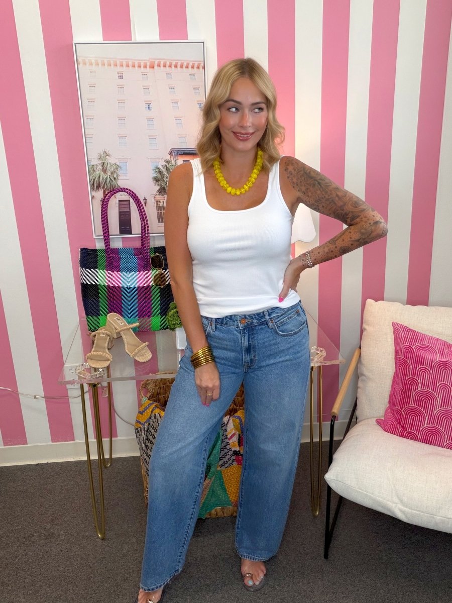 Woman posing in a room with pink and white striped walls, colorful bag, and furniture.