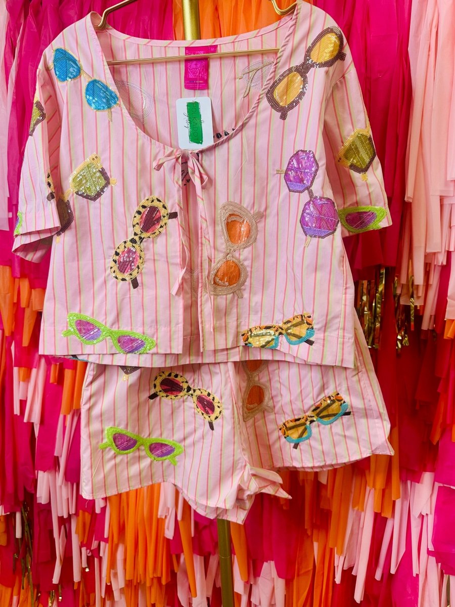 Colorful outfit with sunglasses and flower patterns on a hanger against a vibrant background