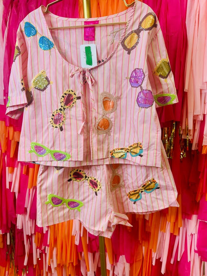 Colorful outfit with sunglasses and flower patterns on a hanger against a vibrant background