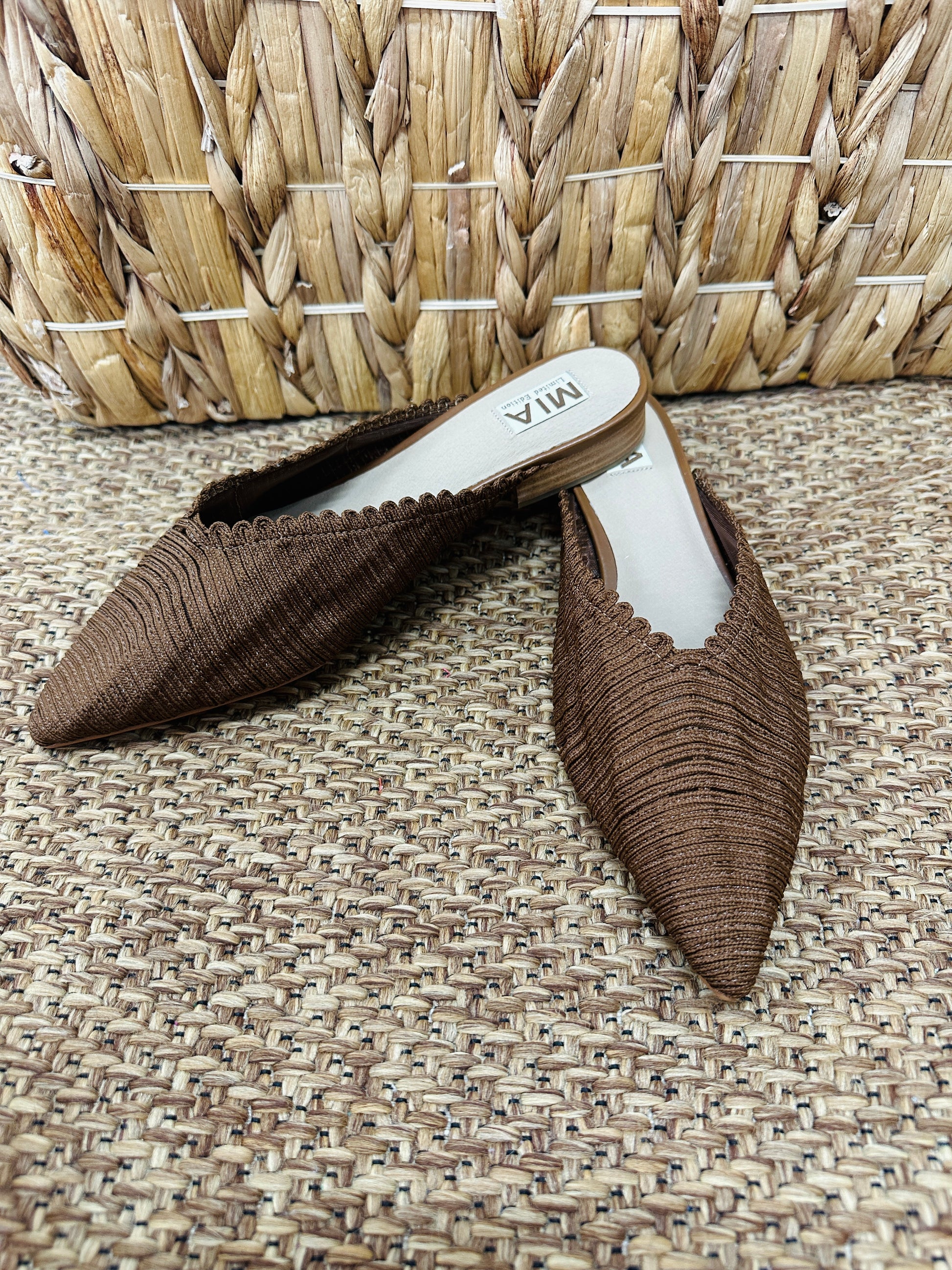 Pair of brown pointed-toe shoes on a textured surface with a woven basket in the background.