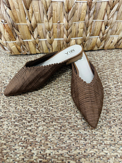 Pair of brown pointed-toe shoes on a textured surface with a woven basket in the background.