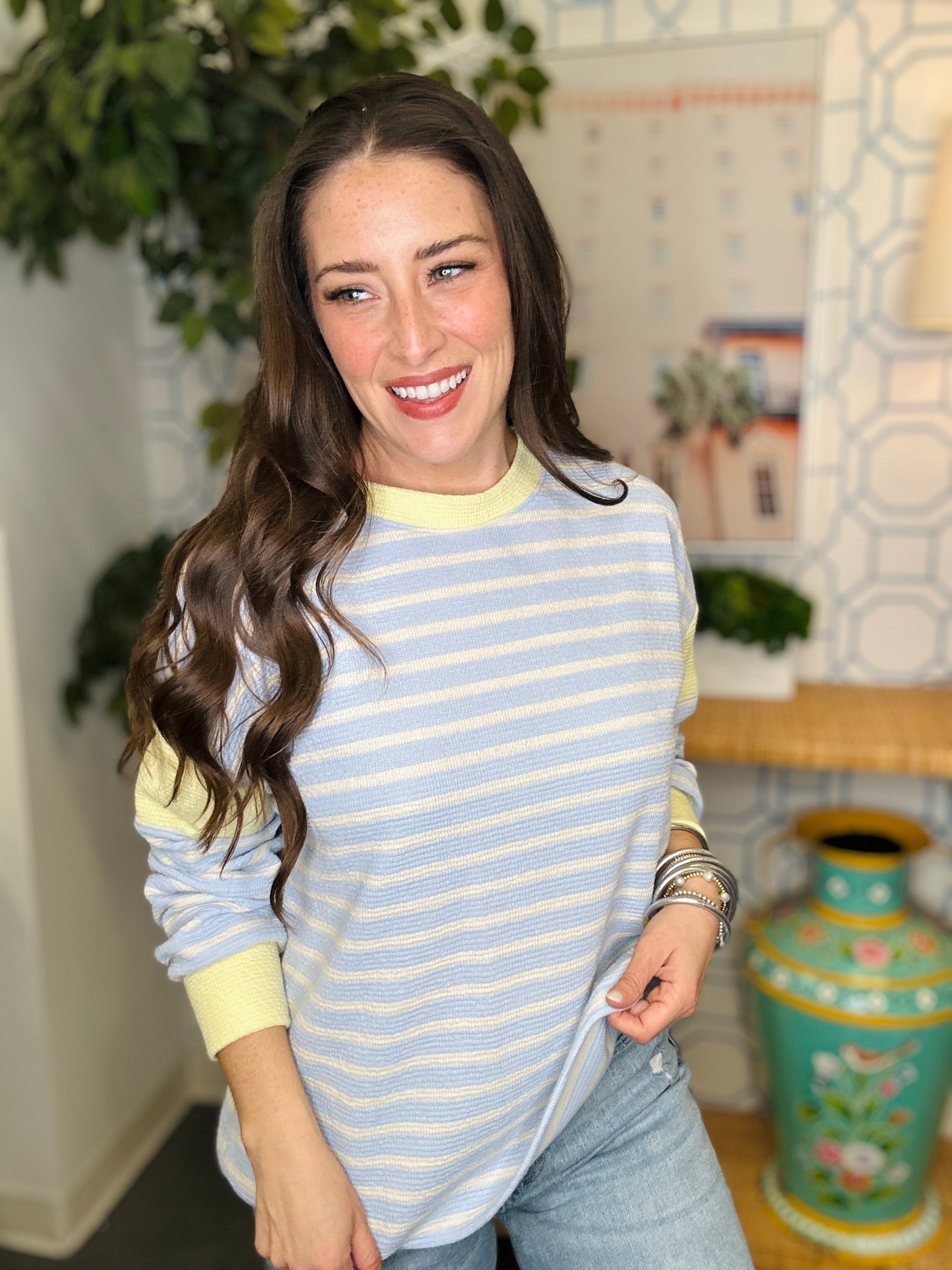 Woman wearing a light blue and yellow striped sweater in a home setting with plants and decor.