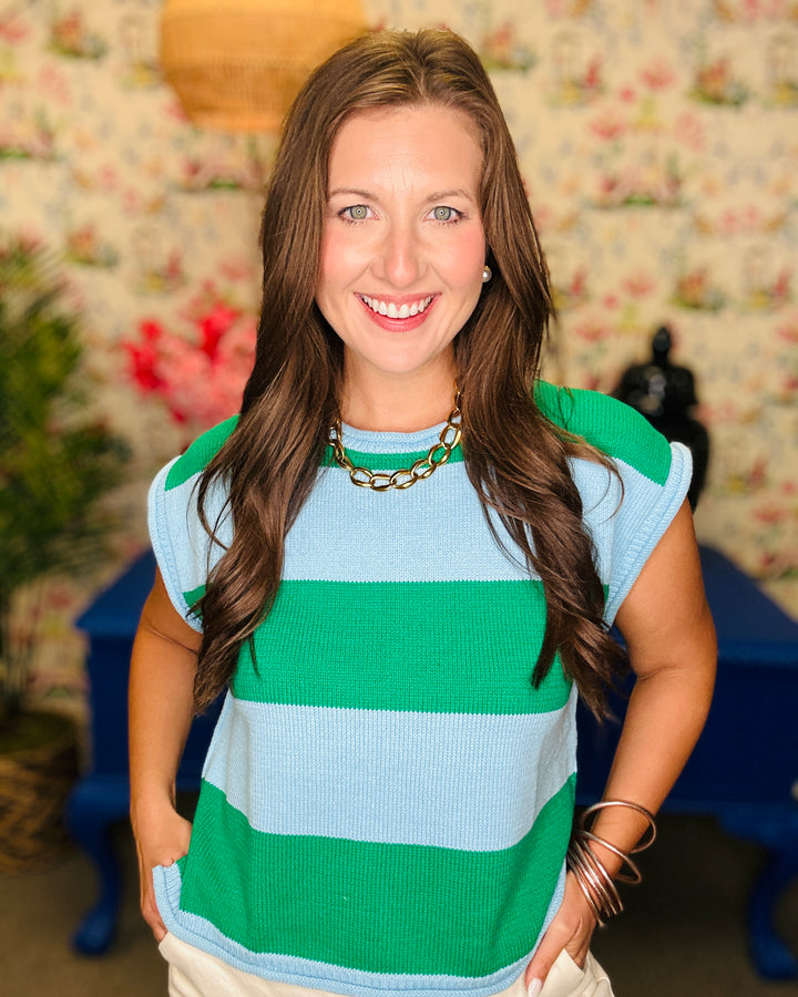 Woman wearing a green and blue striped shirt with a floral wall in the background