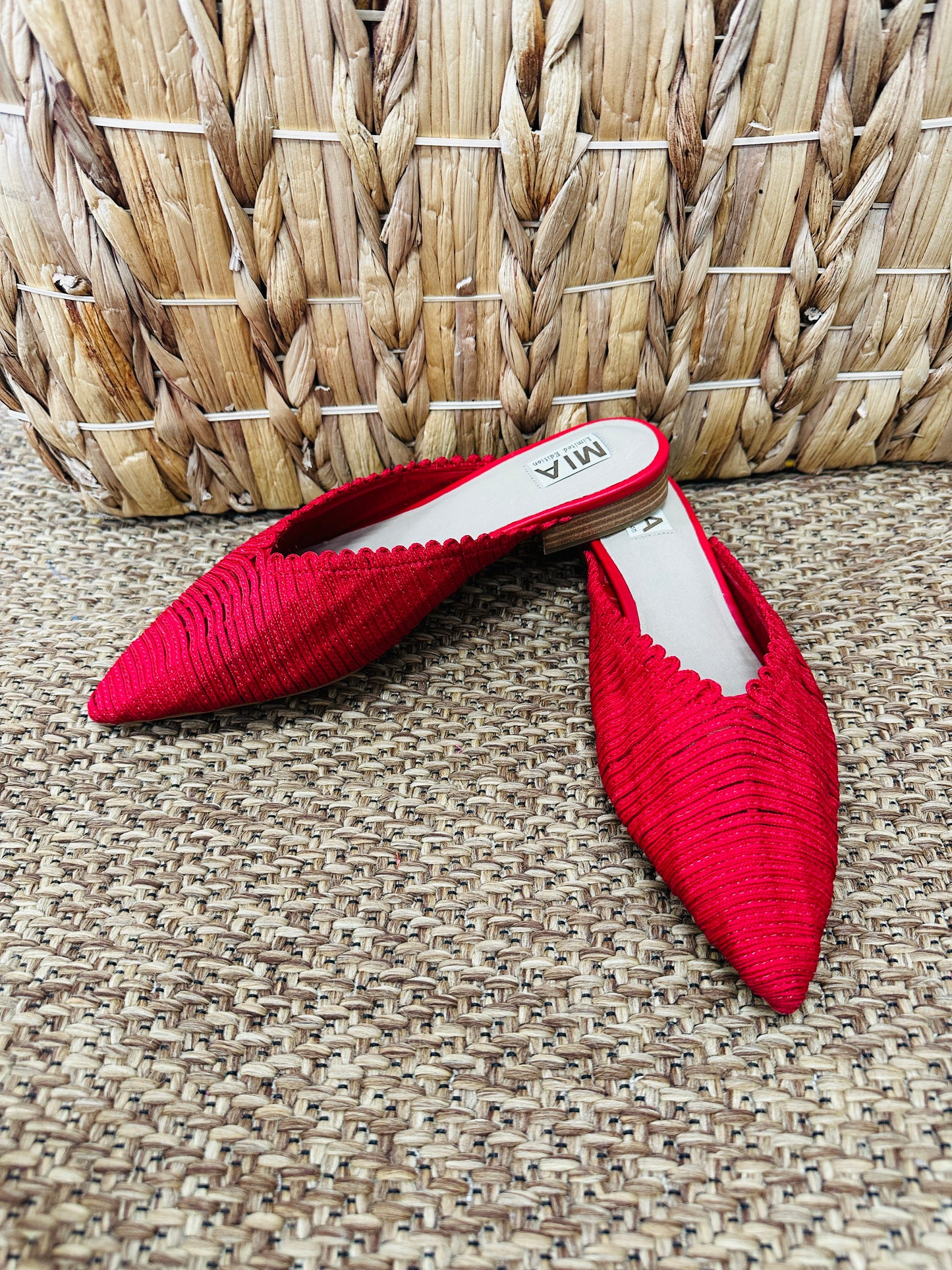 Red pointed-toe shoes on a textured surface with a woven basket in the background