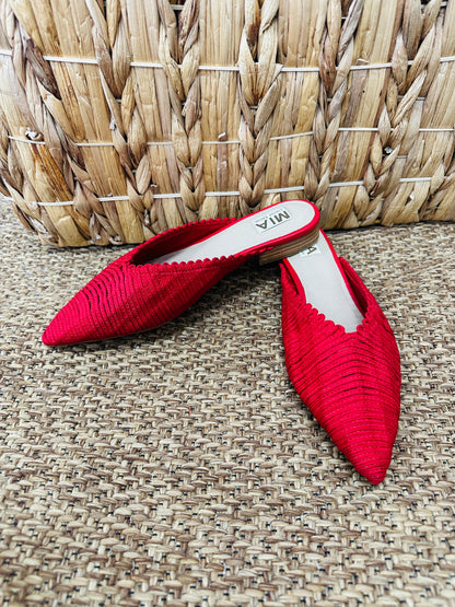 Red pointed-toe shoes on a textured surface with a woven basket in the background