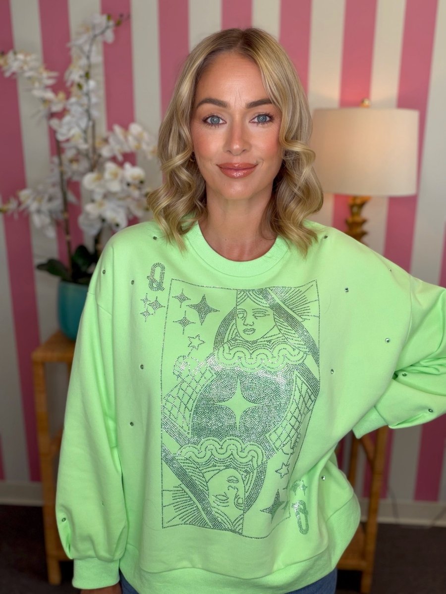 A woman wearing a neon green crewneck sweatshirt with a dark graphic print of Queen of Cups tarot card imagery, posed in front of a pink and white striped wall.
