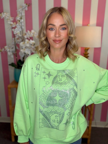 A woman wearing a neon green crewneck sweatshirt with a dark graphic print of Queen of Cups tarot card imagery, posed in front of a pink and white striped wall.