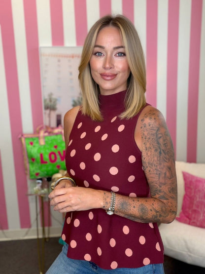 Woman wearing a polka dot top in a room with pink and white striped wallpaper.