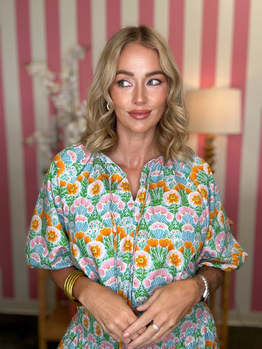 Woman wearing a colorful floral dress in a room with striped wallpaper.