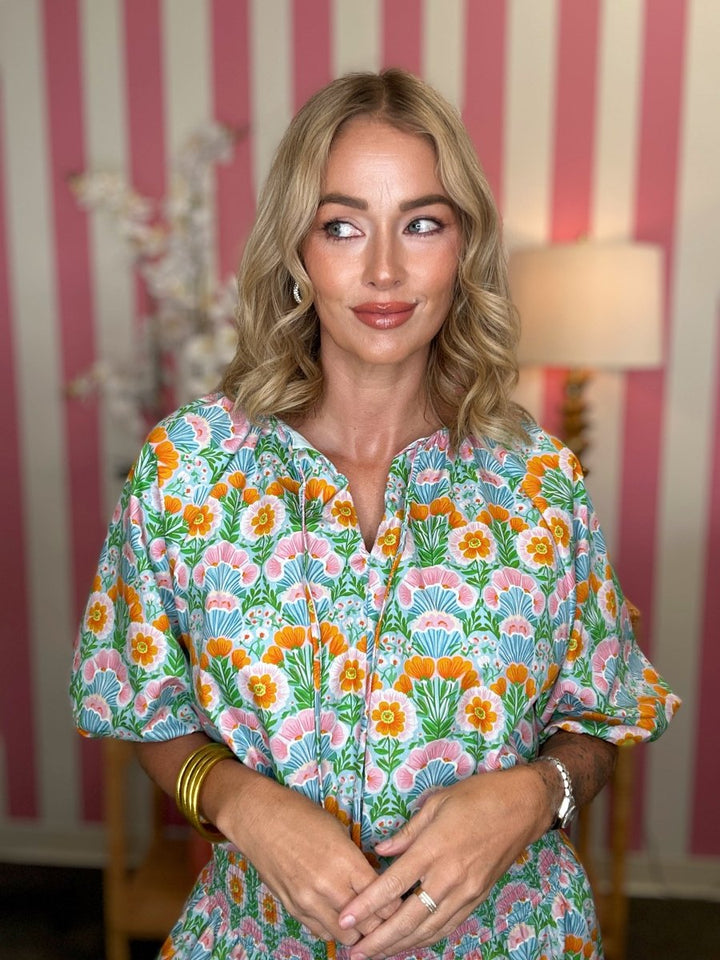 Woman wearing a colorful floral dress in a room with striped wallpaper.