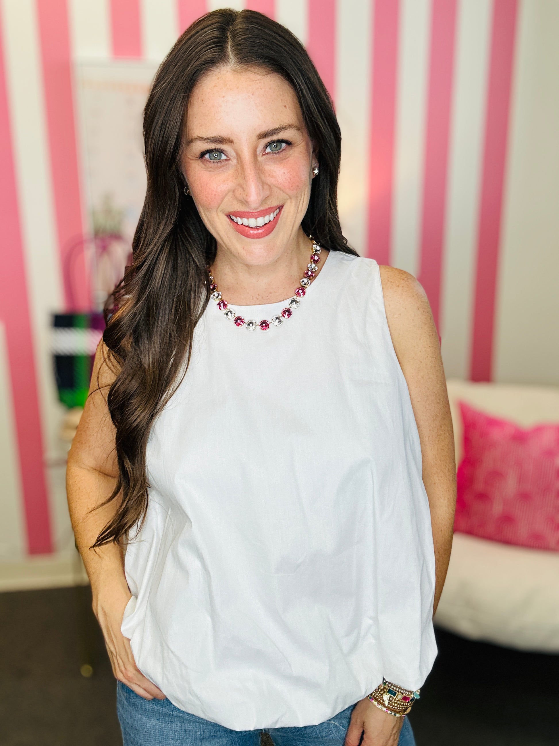Woman wearing a white sleeveless top with a pink and white striped background