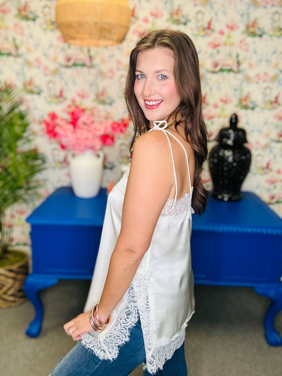 Woman wearing a white lace top with a floral wall and blue furniture in the background