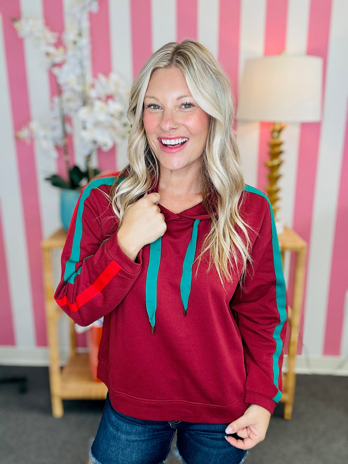 Woman wearing a red hoodie with teal accents in a room with pink and white striped walls.