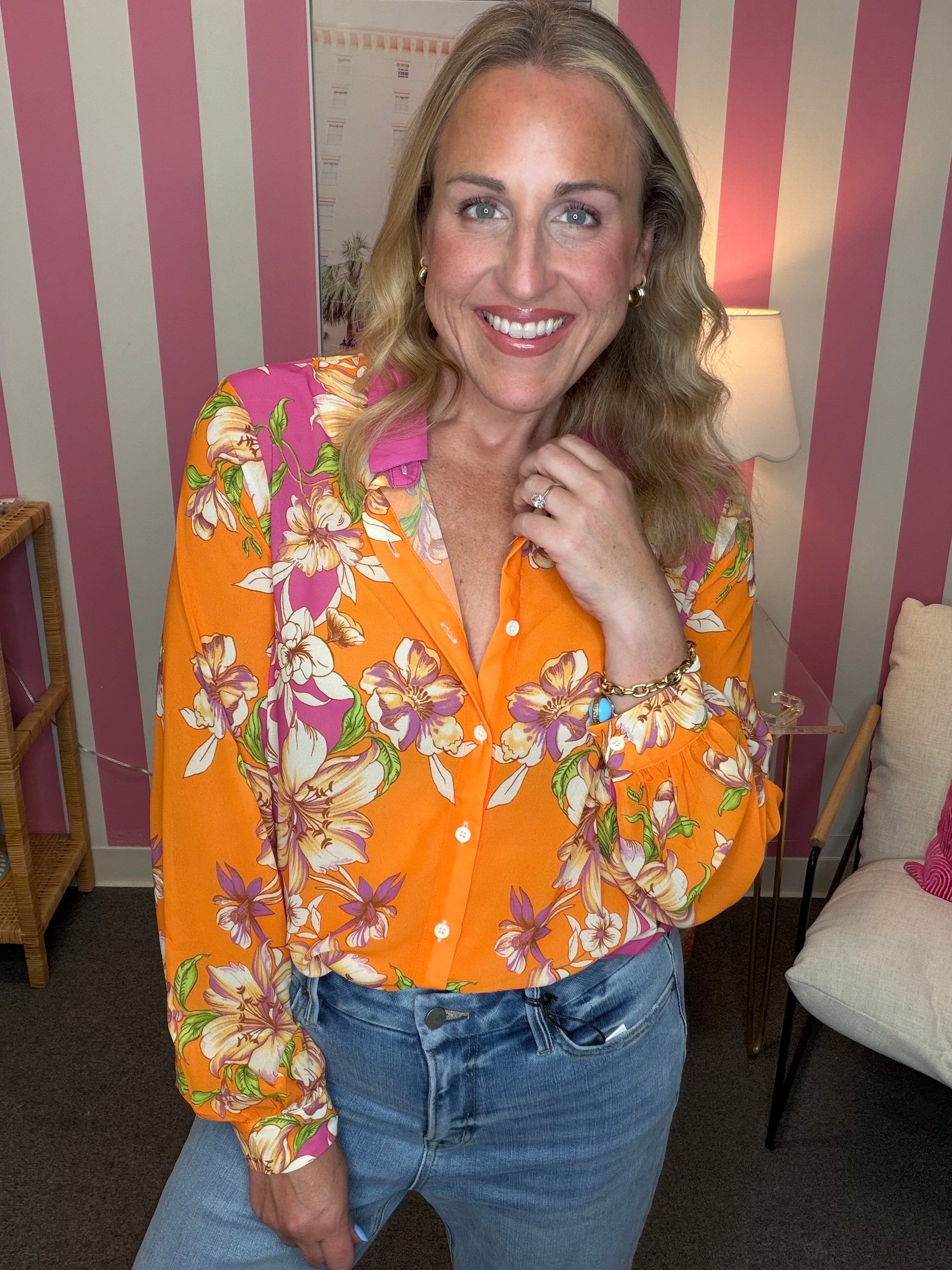 Woman wearing a colorful floral shirt in a room with striped walls.