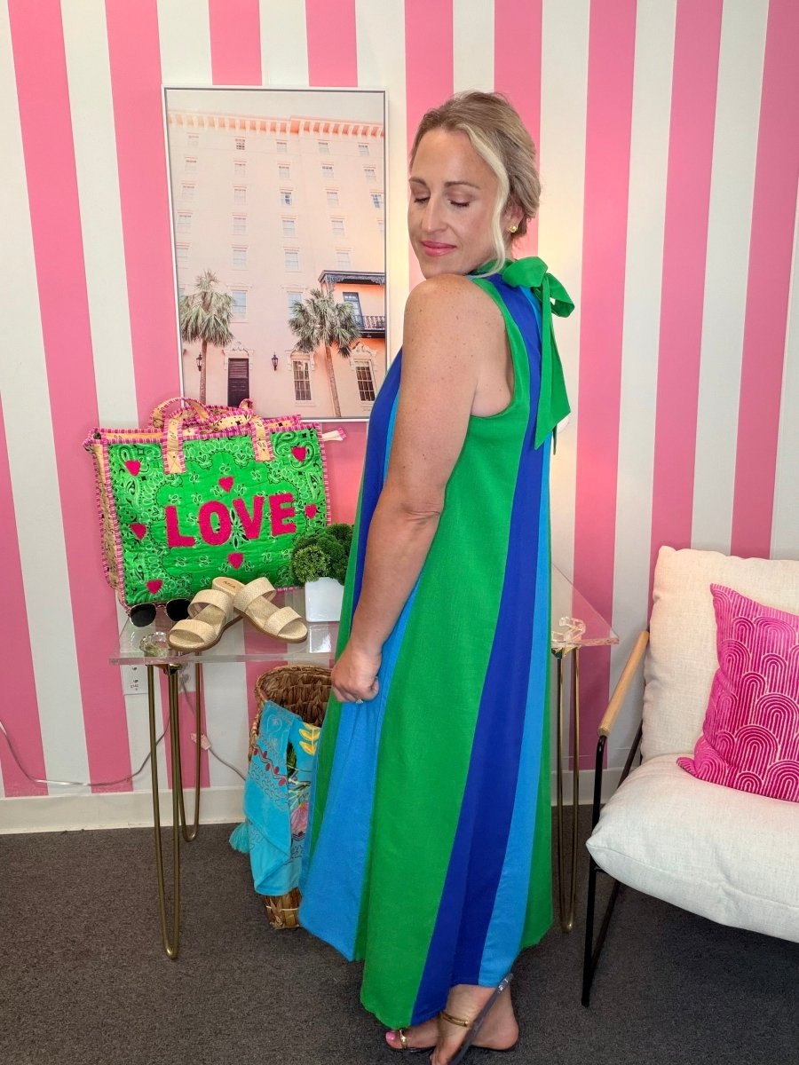 Woman in a colorful dress standing in a room with pink and white striped walls, a calendar, and a couch.