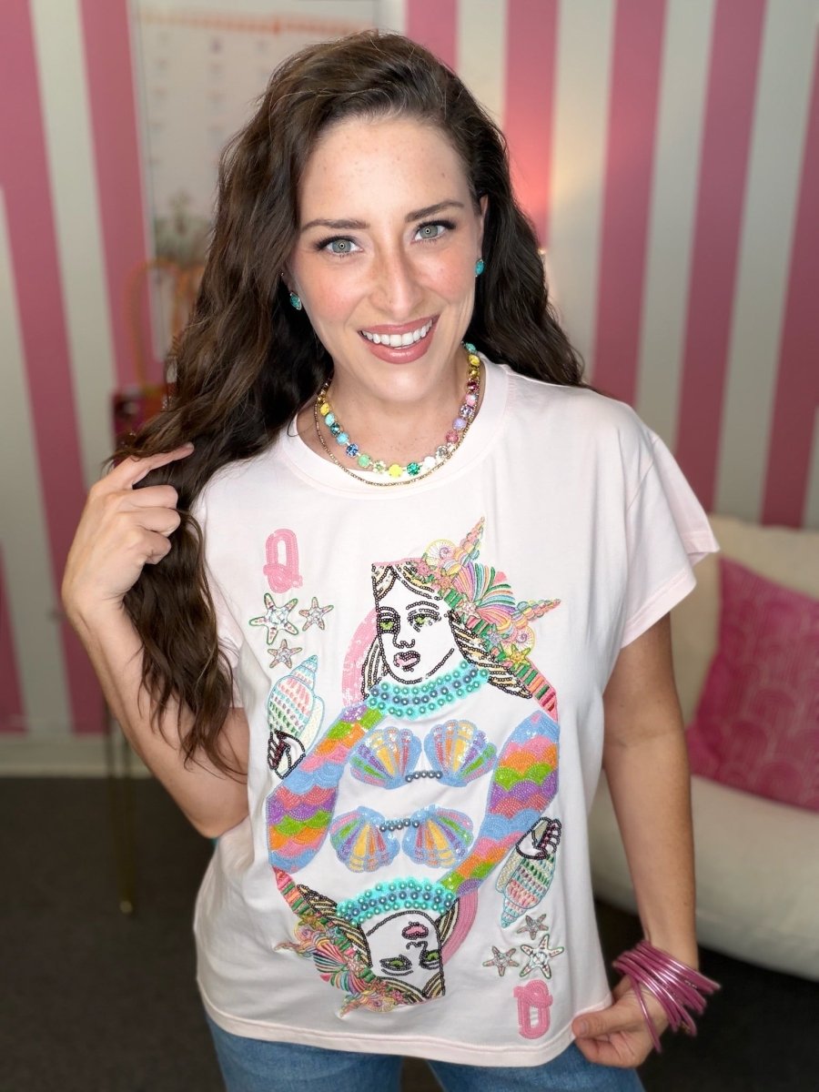 Woman wearing a white t-shirt with colorful graphic design in a room with pink and white striped wallpaper.