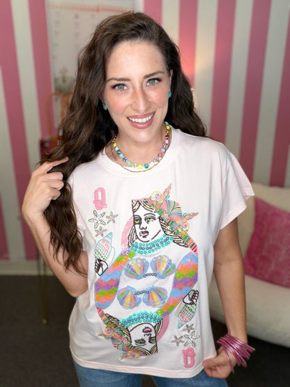 Woman wearing a white t-shirt with colorful graphic design in a room with pink and white striped wallpaper.